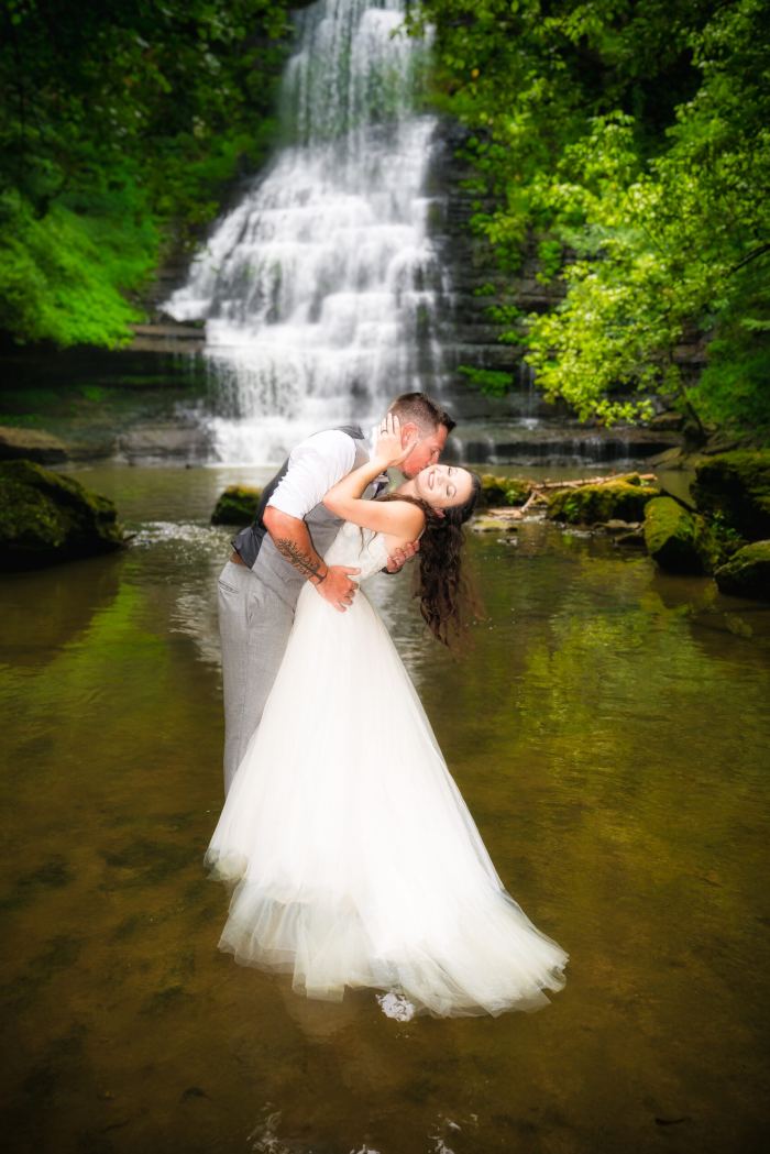 Groom holds his bride in front of a private waterfall